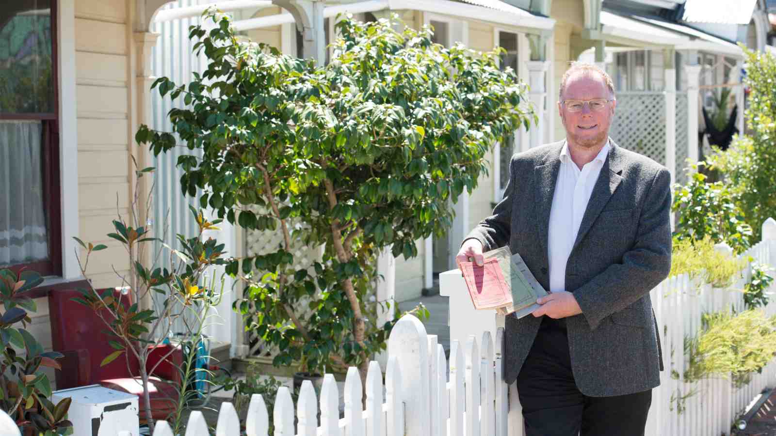 Nigel Isaacs holding building act books outside Victorian style homes in Wellington