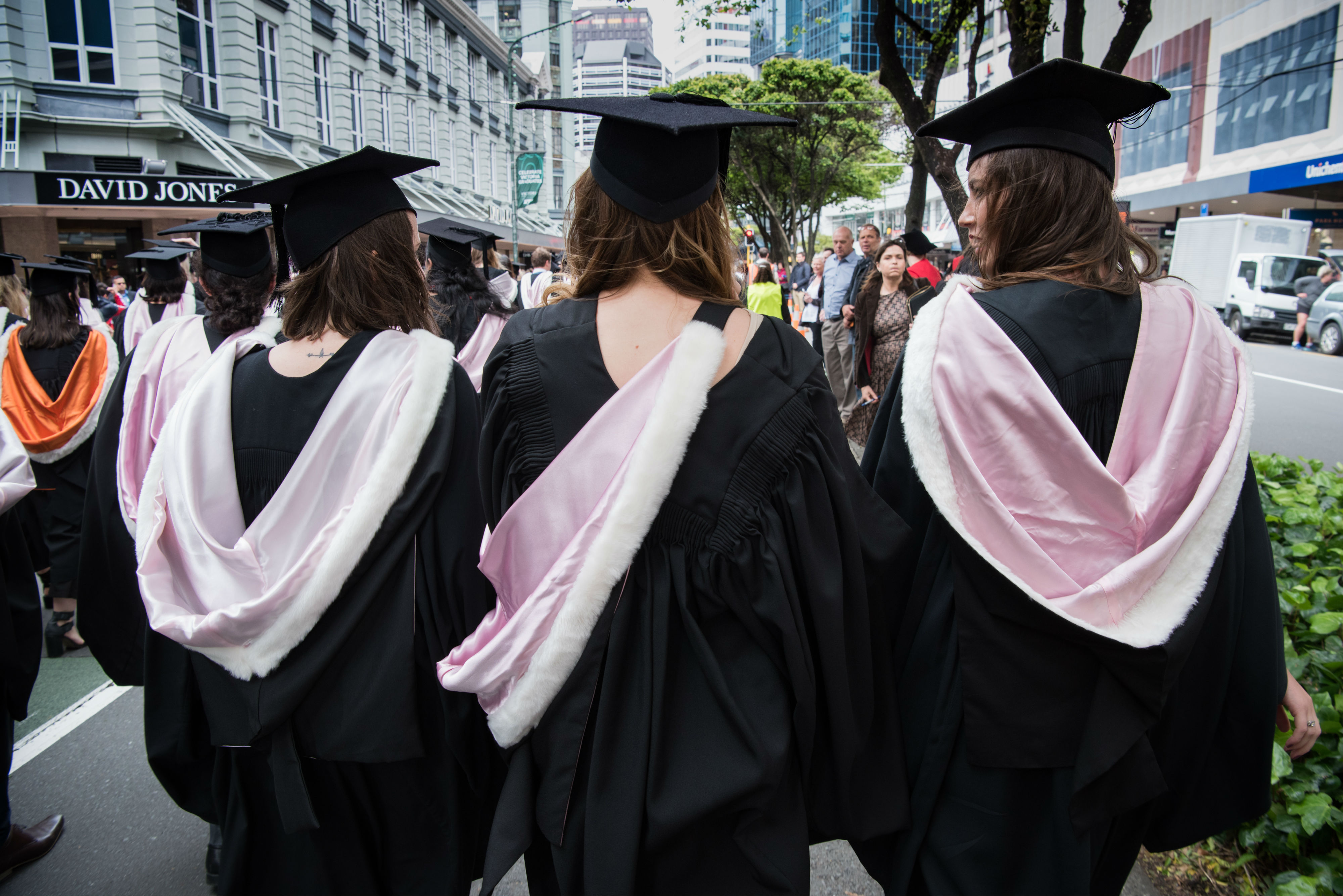 Three women marching with thier backs to the camera wearing Humanities robes.