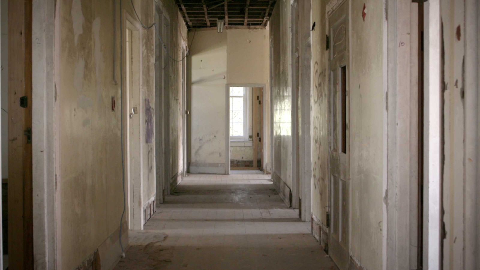 A still from 'Humans' – A hallway with doors several doors in a dilapidated building with dusty wooden floors.