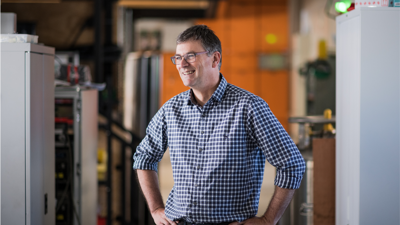 Man with hands on hips, wearing blue checked shirt, in scientific background