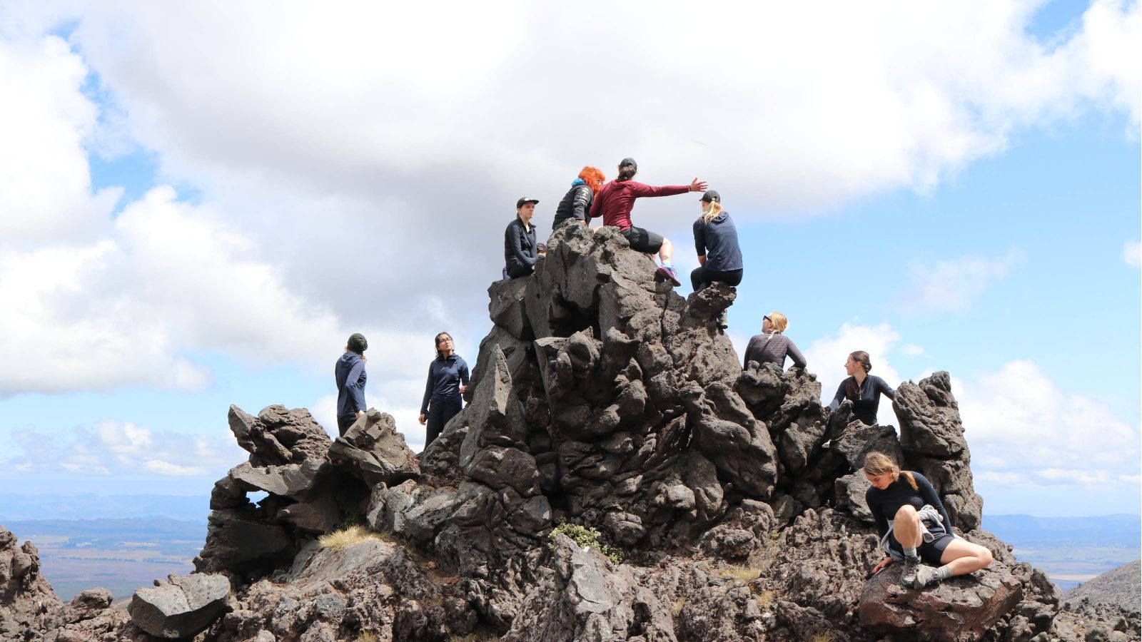 A group of girls in outdoor gear sitting on a rock outcrop on Mt Ruapehu