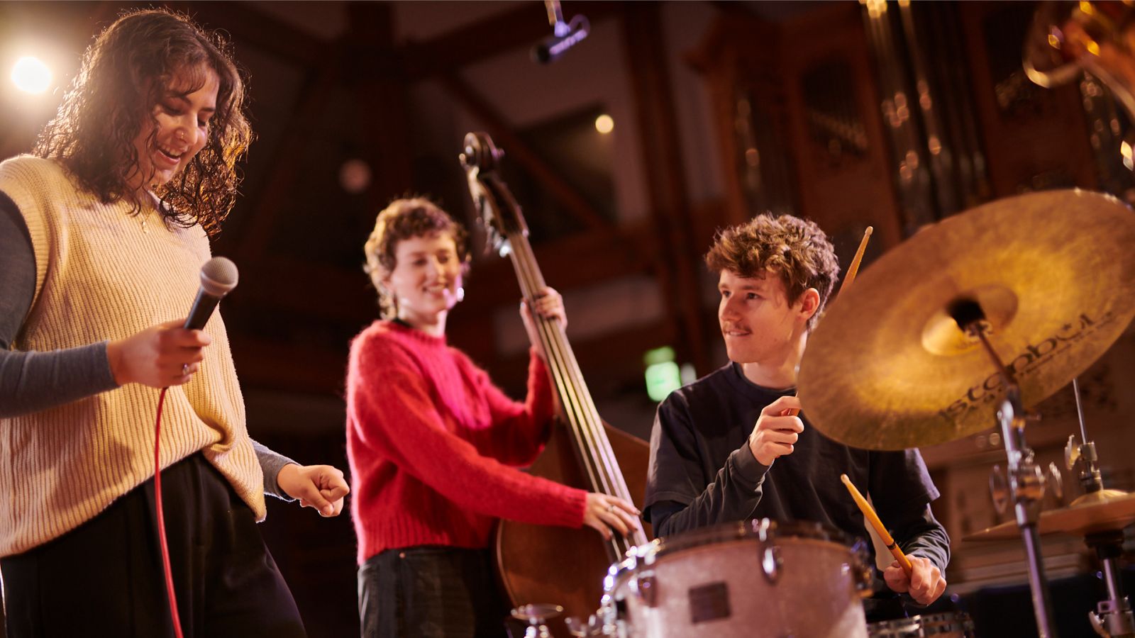 A singer, double bass player and drummer rehearse together