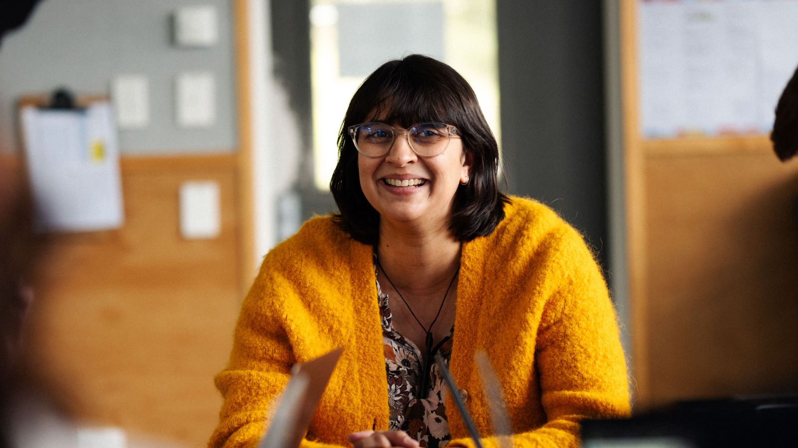 Student wearing a yellow cardigan and glasses smiling into the camera