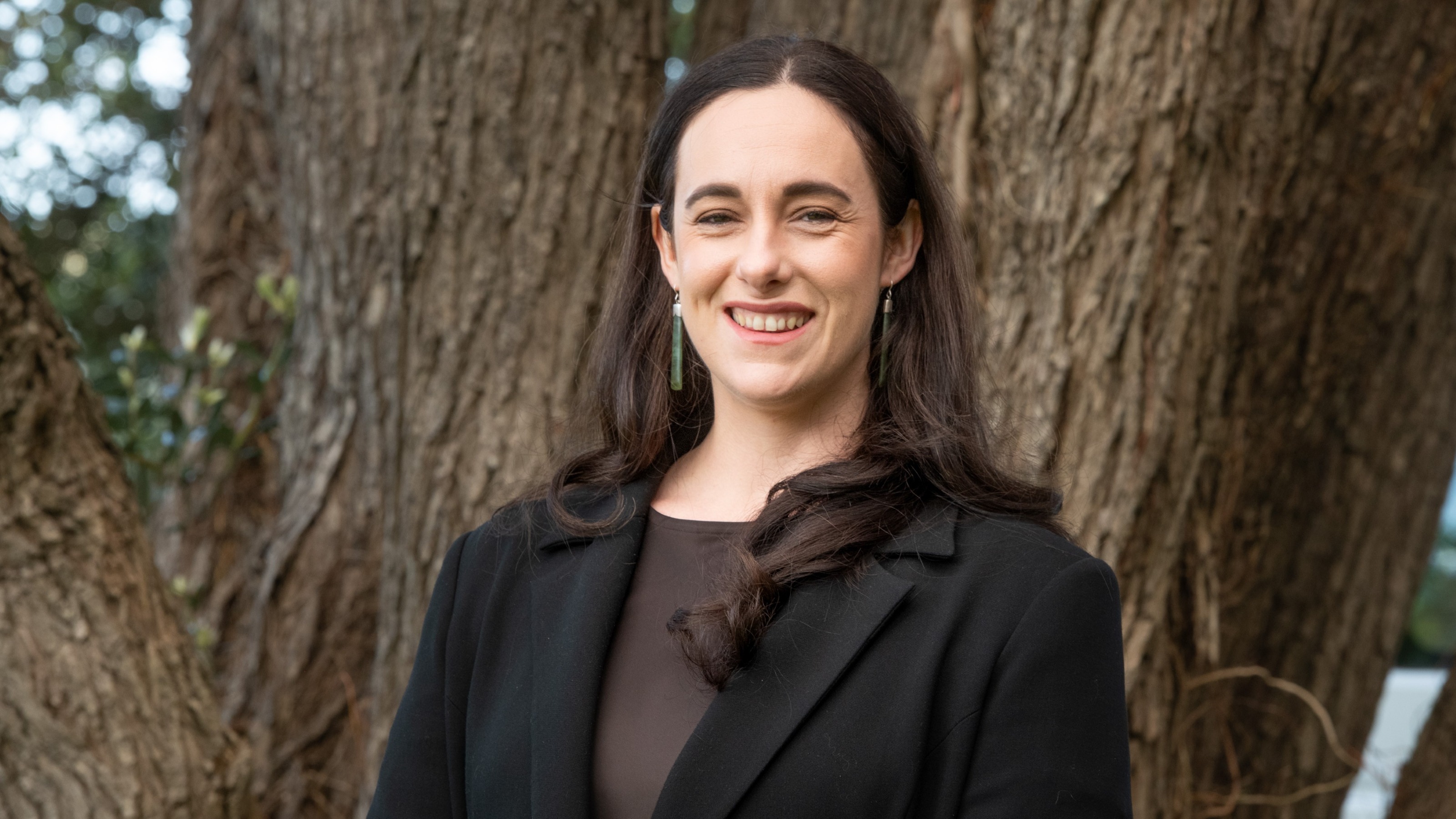 Associate Professor Lara Greaves stands in front of the trunk of a large tree. 