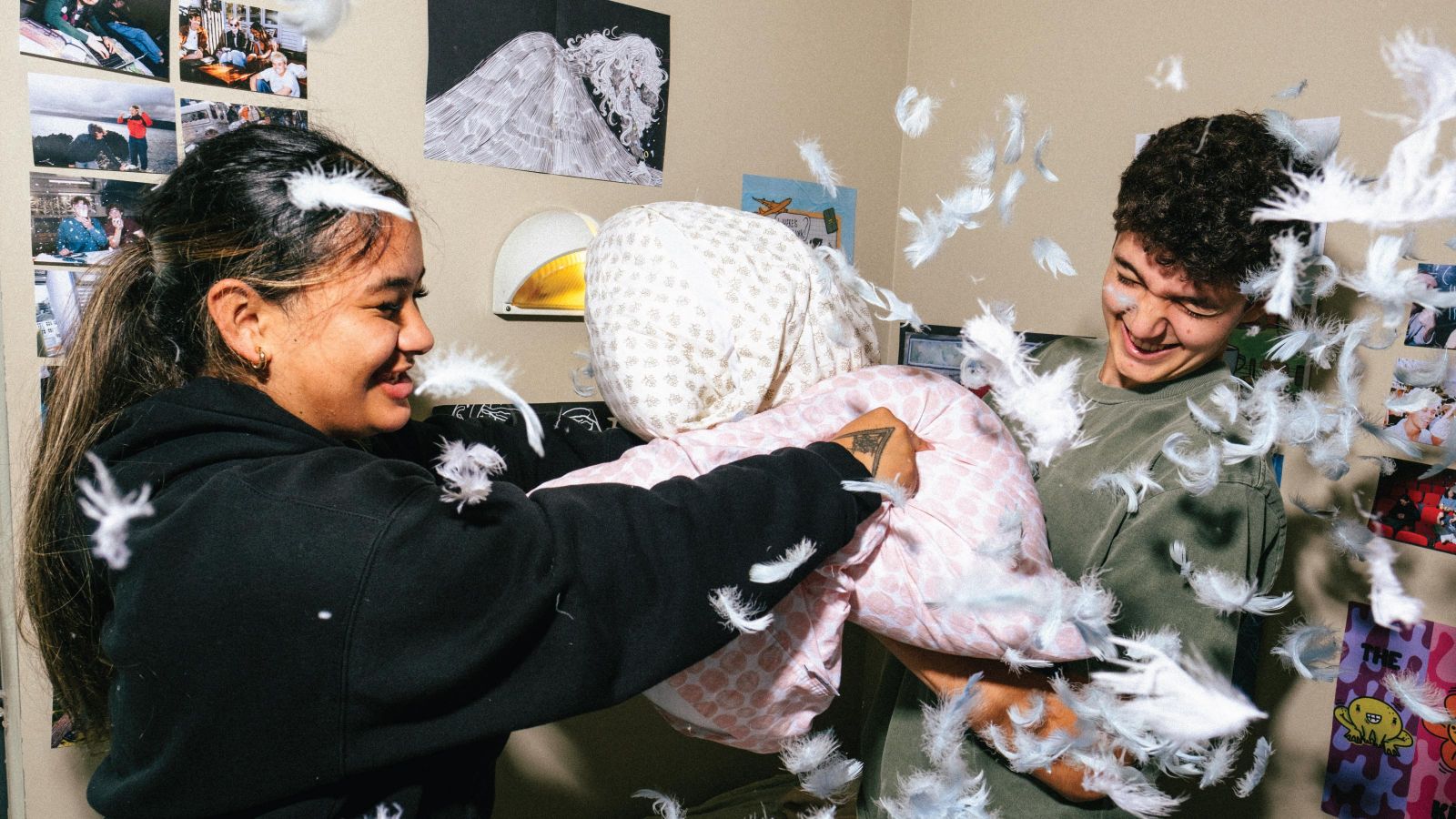 Two students smiling and having a pillow fight with feathers everywhere