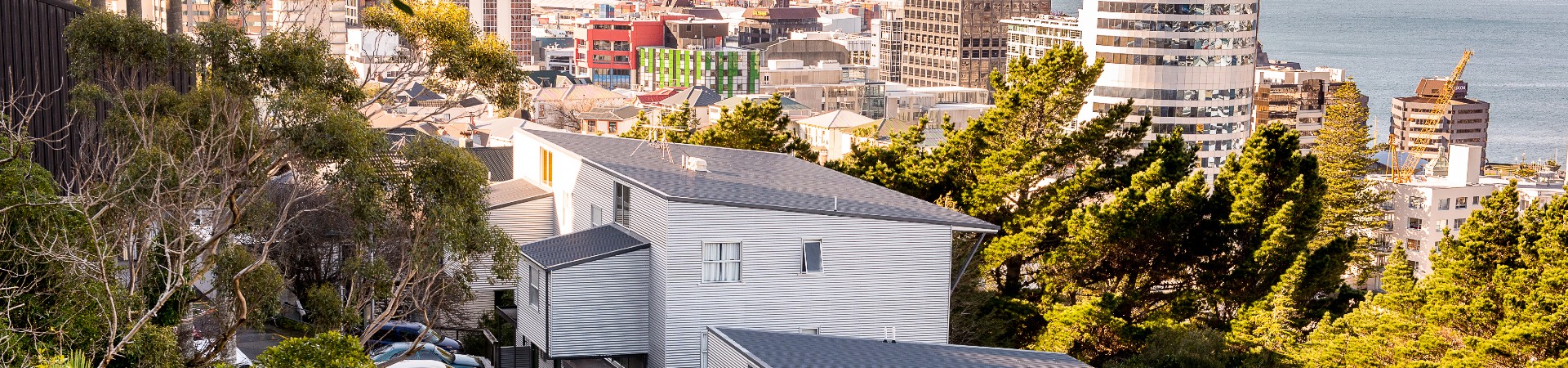 Grey corrugated 2-story apartment building with windows. Trees surround building, overlooks the city and harbour.