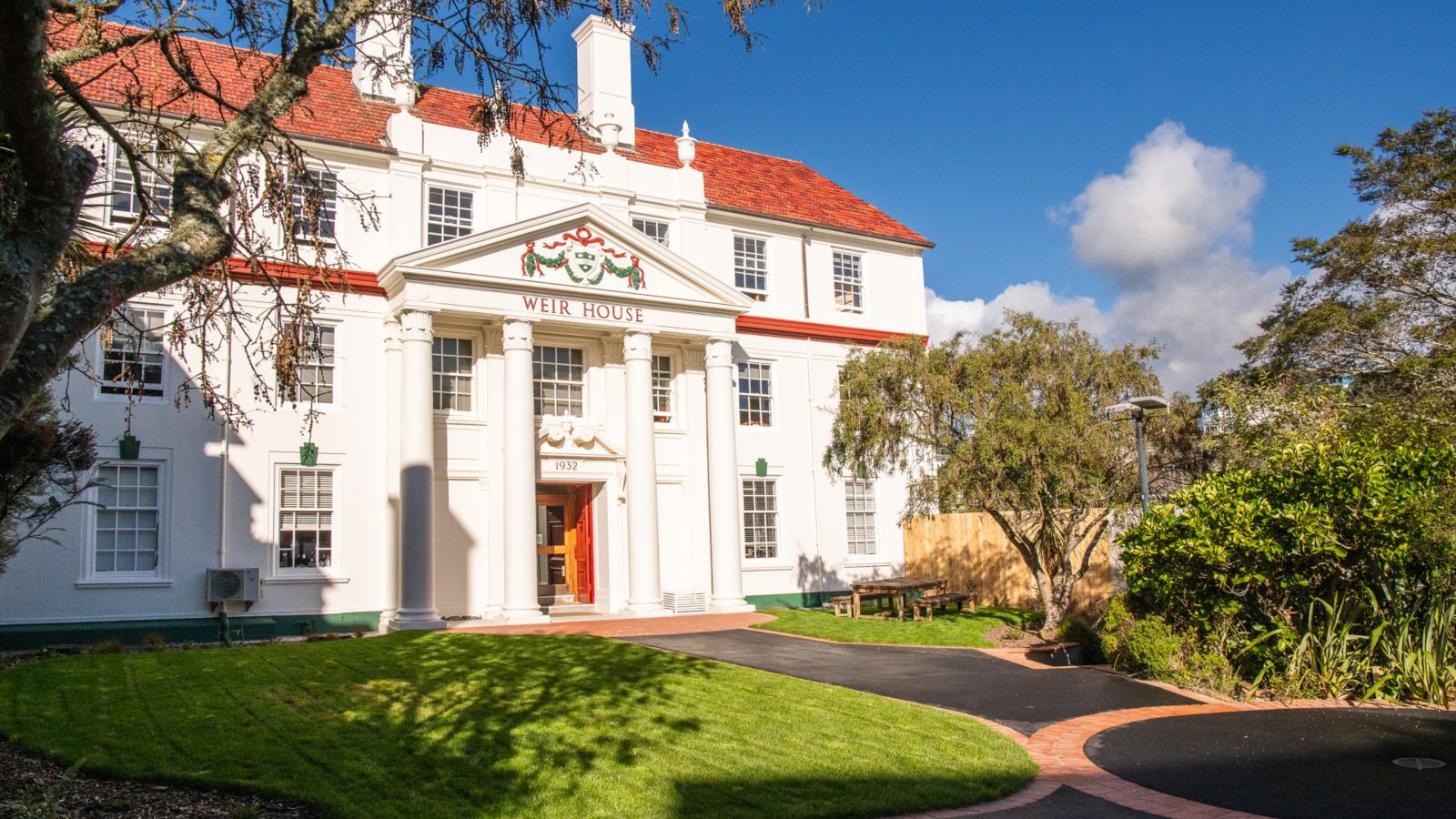 Circular green lawn in front of white building with columns and red tile roof. A picnic table and chairs are on the lawn outside. 