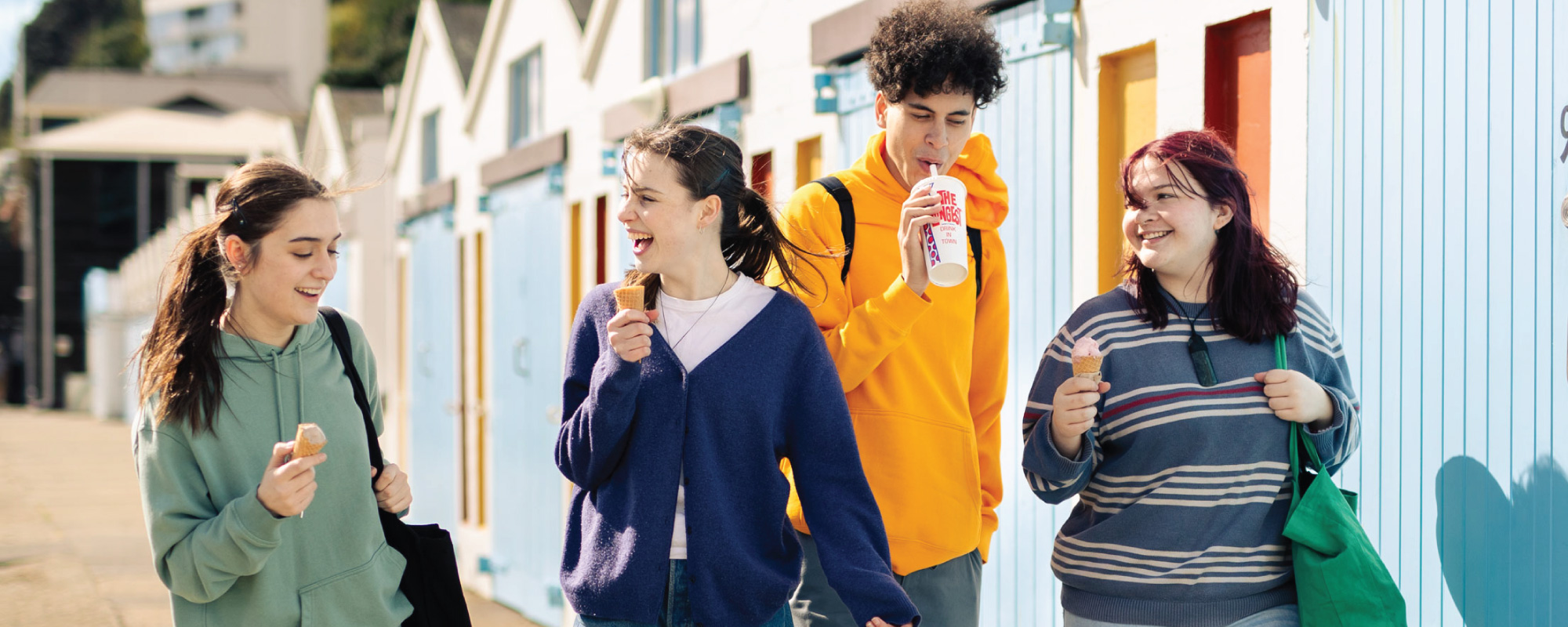 A group of four students walking by the boatsheds near Oriental Bay, three with ice creams, one with a milkshake.