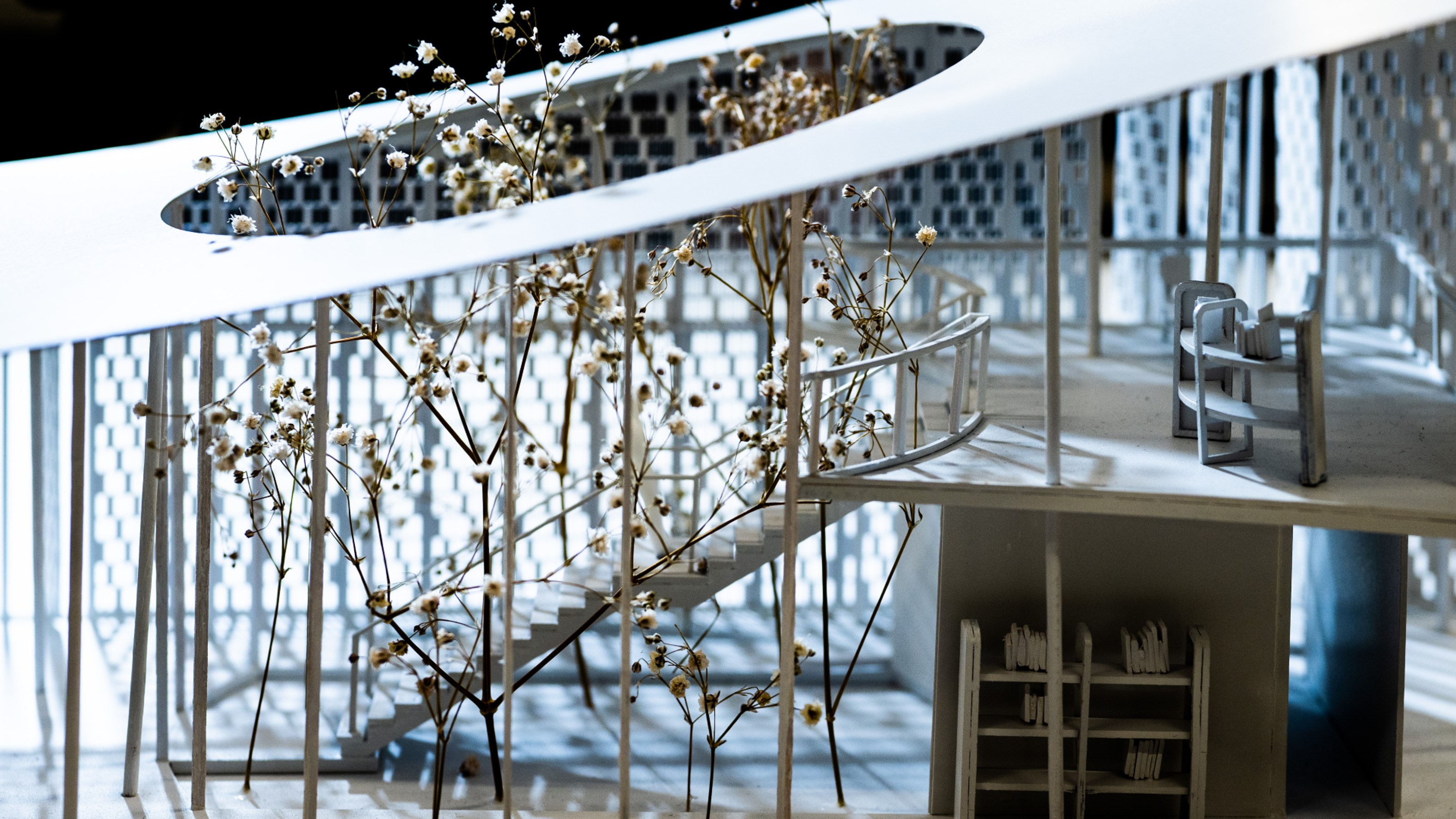 Close up view from outside of architectural model showing the side of the indoor staircase and a book shelf surrounded by trees