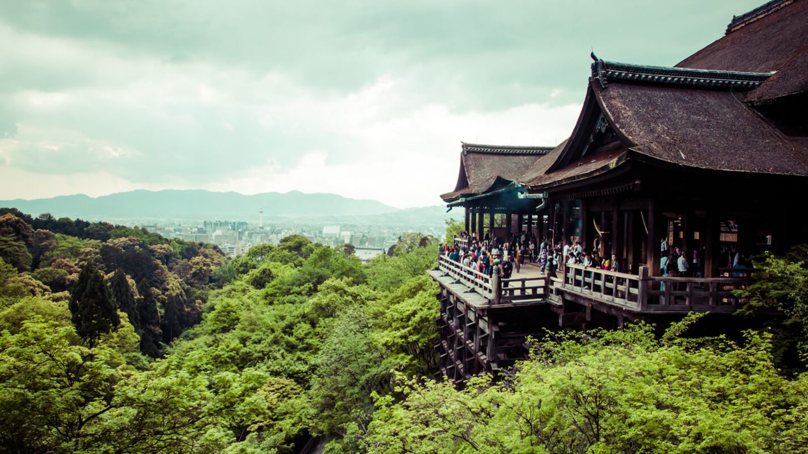Old Japanese hillside temple with trees in foreground and city in distance