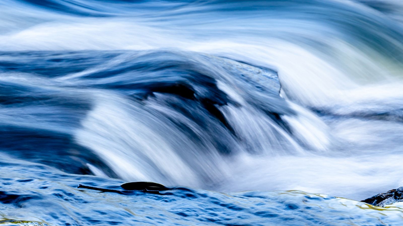 Blue water rushing over rocks with stick floating in foreground
