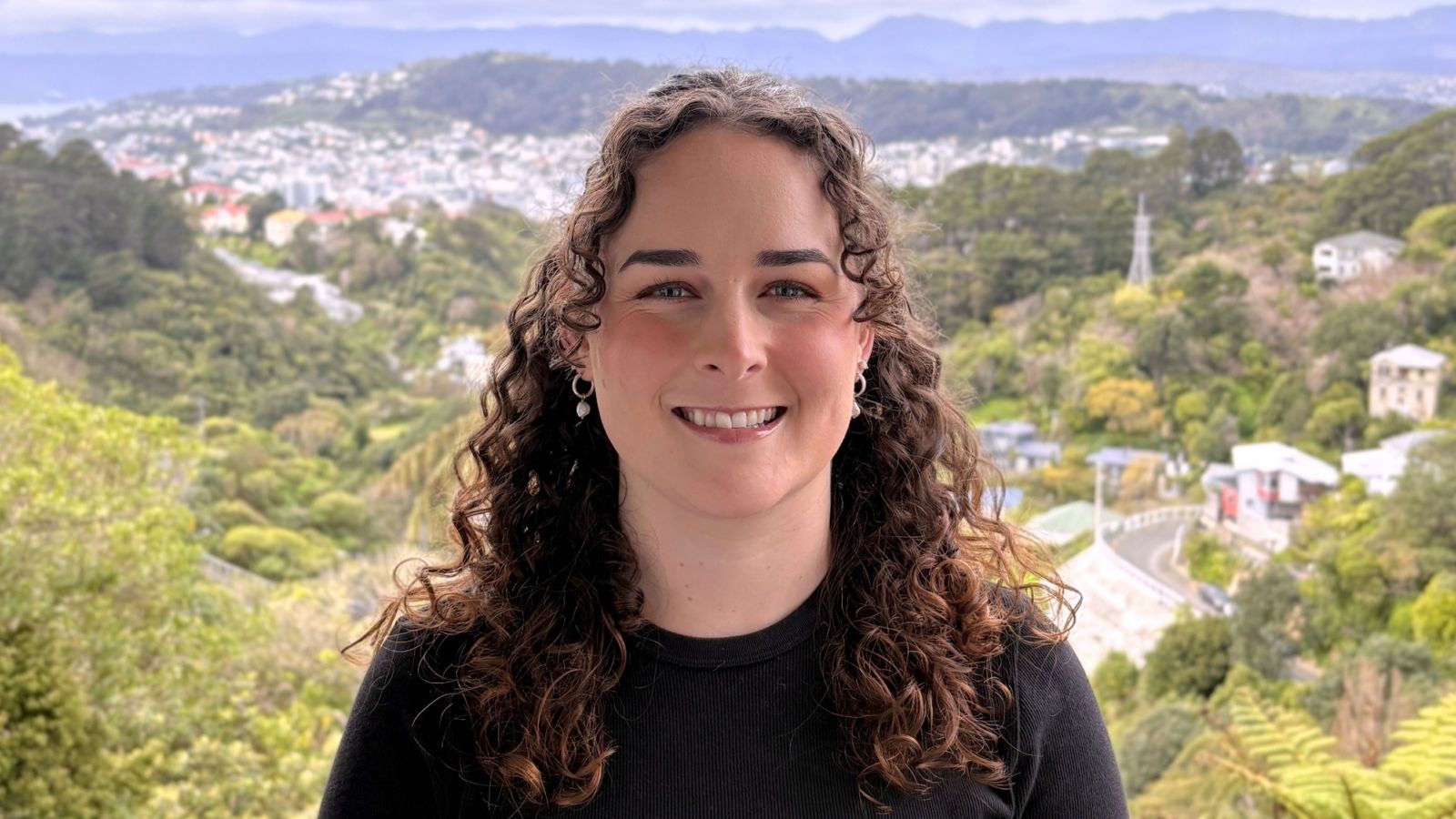 A head and shoulders image of Rochelle Tait with view of Zelandia and Brooklyn Turbine in Wellington in the background. 
