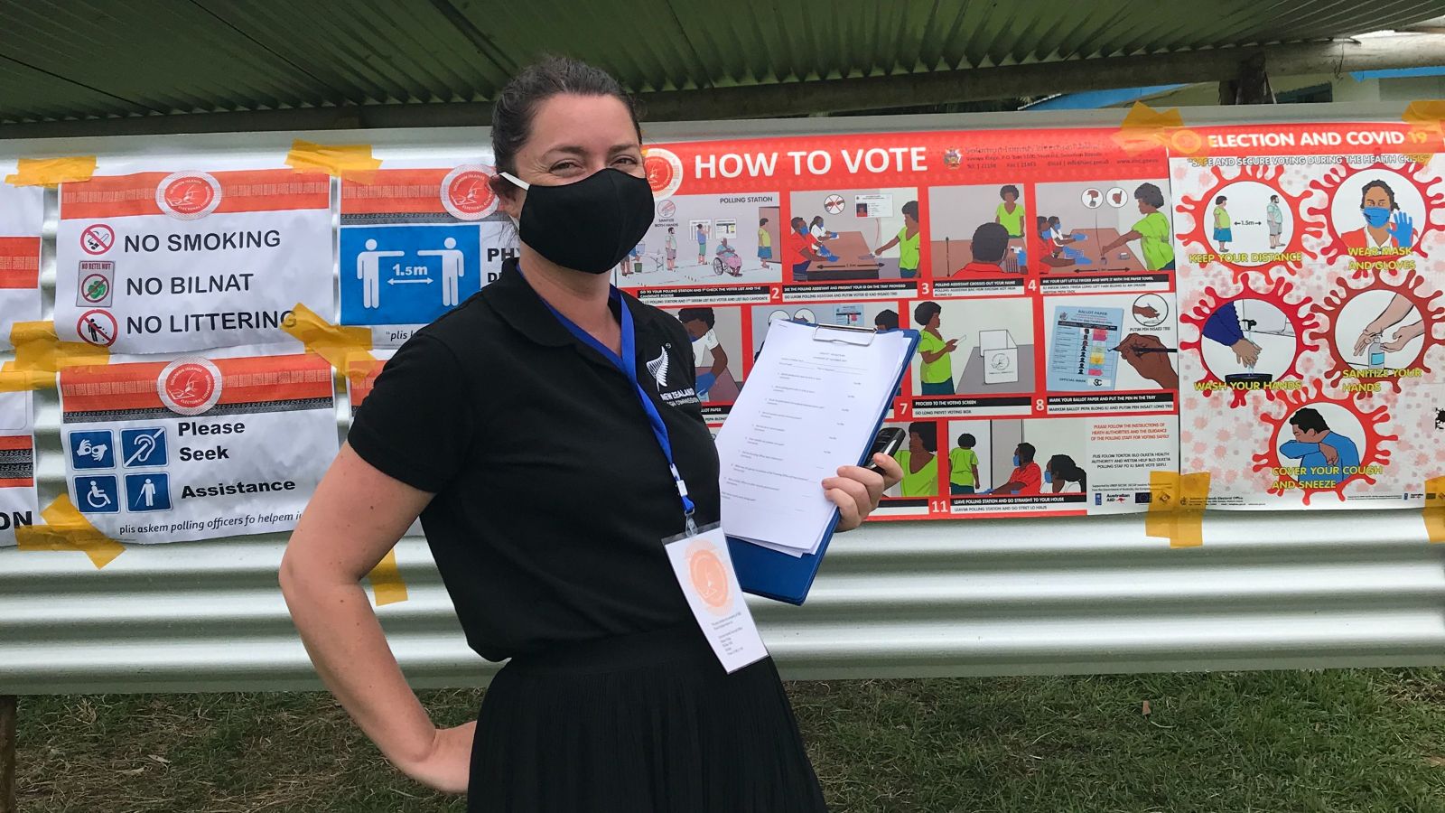 A photo of Hannah during an election monitoring mission in Solomon Islands. Hannah wears a black dress, a black face mask, and carries a clipboard.