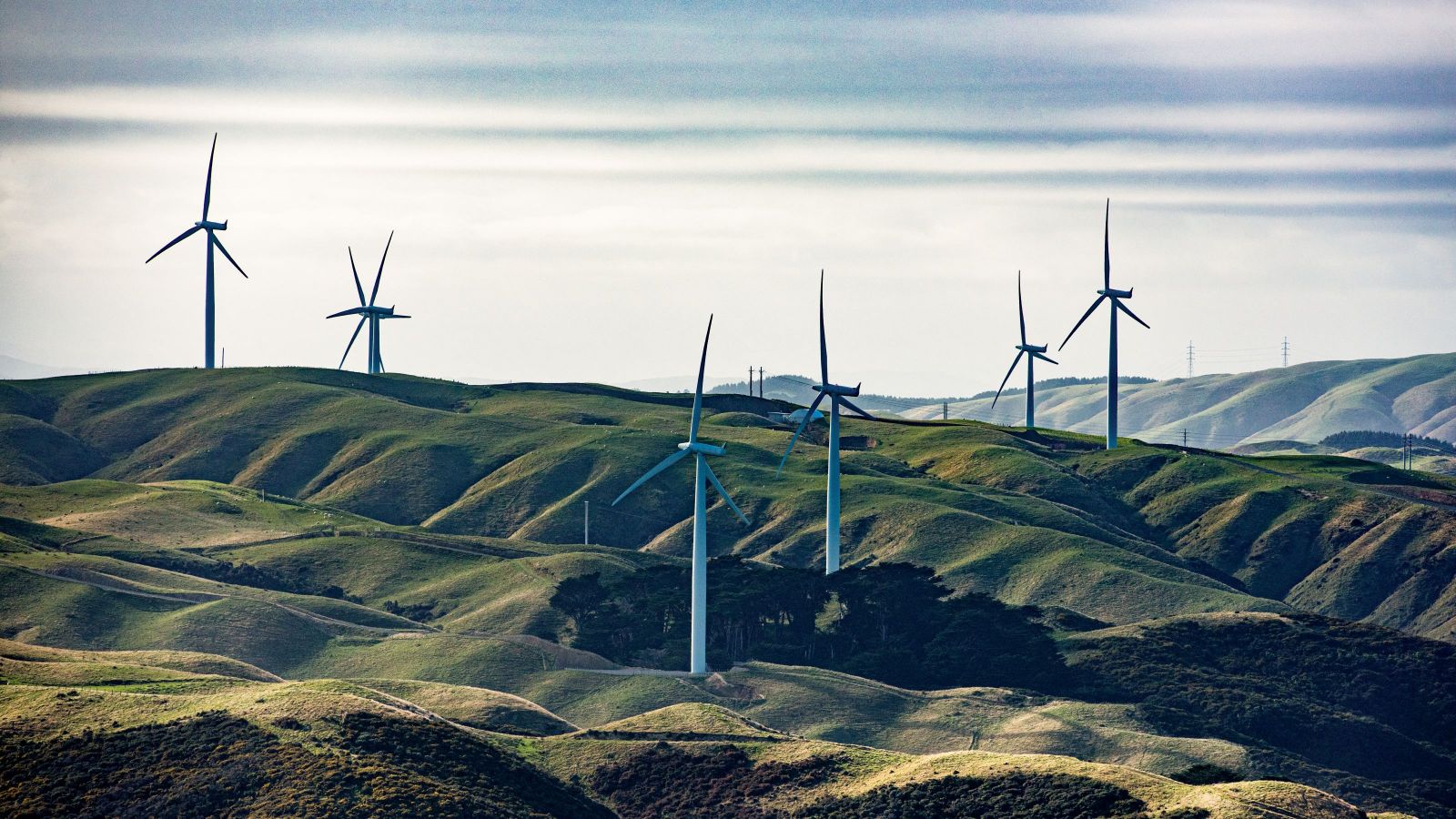 A number of large wind turbines on rolling rural hills under a grey sky