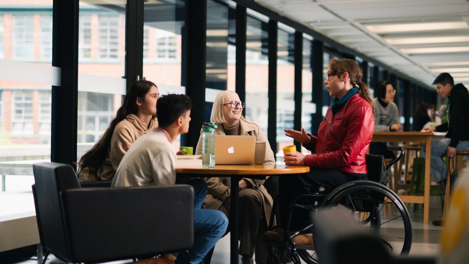A group of students, one using a wheelchair, sitting around a table talking.