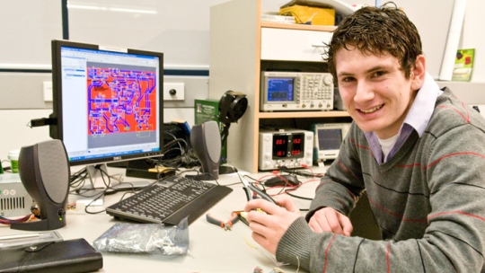 Brendan Vercoelen sits at a desk with a computer and smiles.