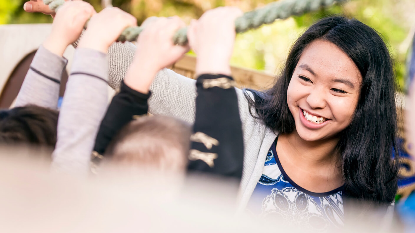 A female trainee teacher with children on playground equipment.