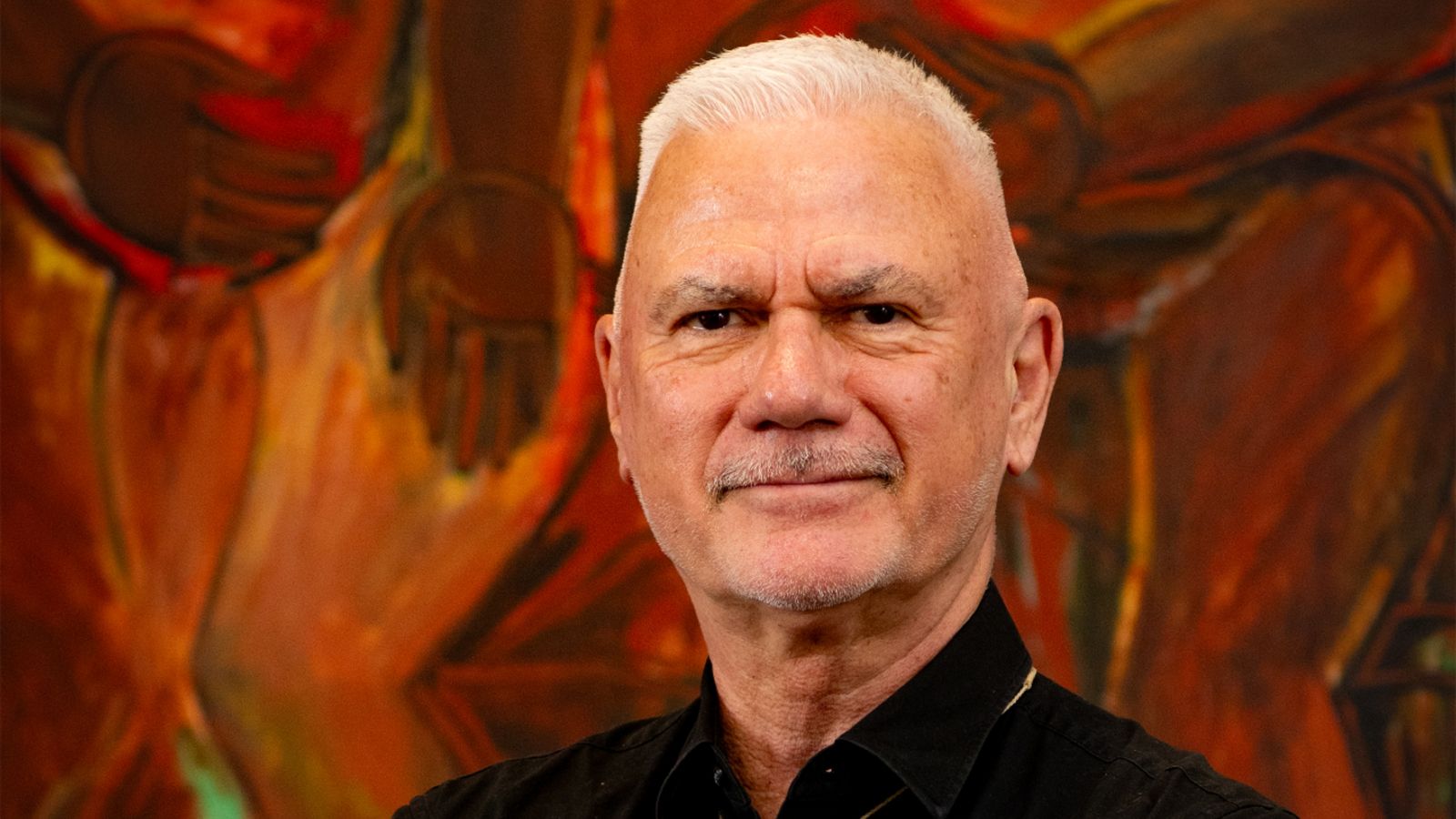 Man with black shirt and grey hair and moustache smiling