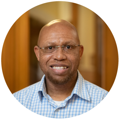 Dark skinned bald man with glasses smiling