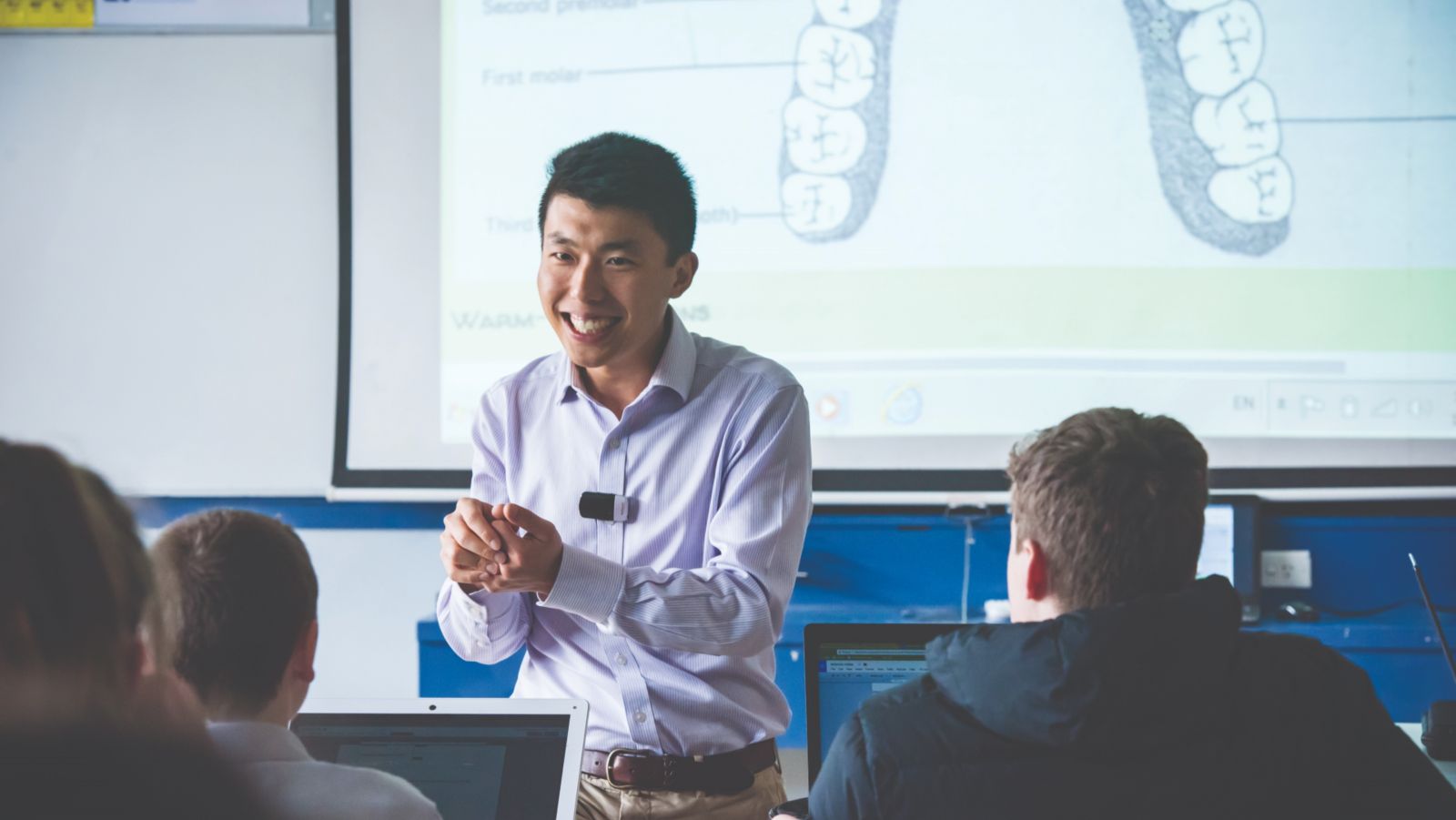 Man in white shirt speaking to a class of students