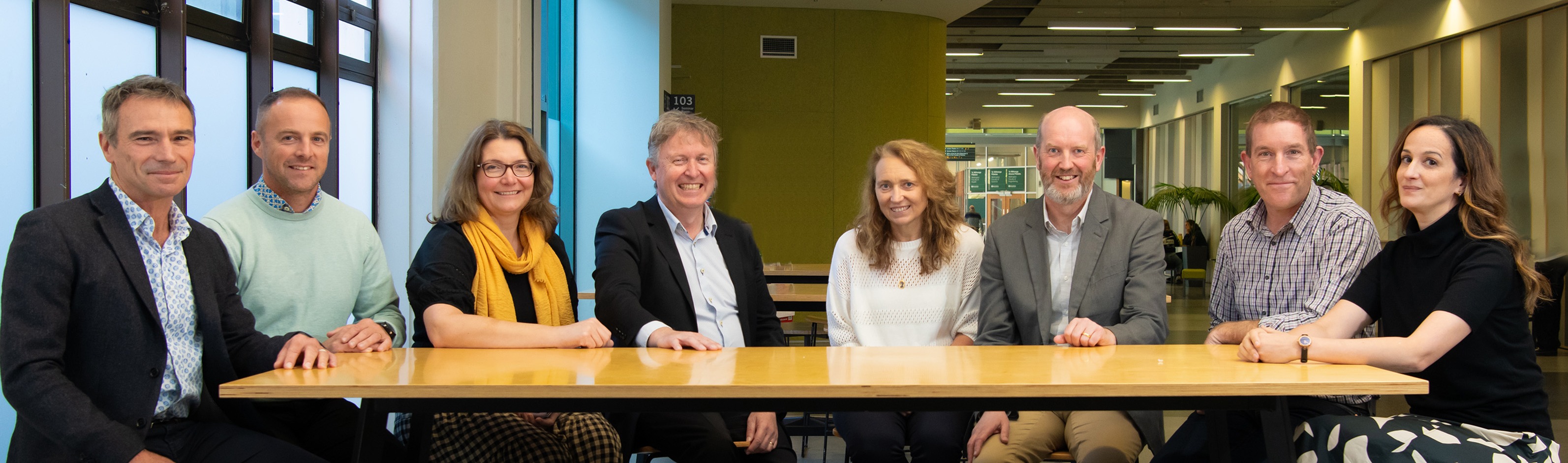 A group of eight people sitting behind a table.