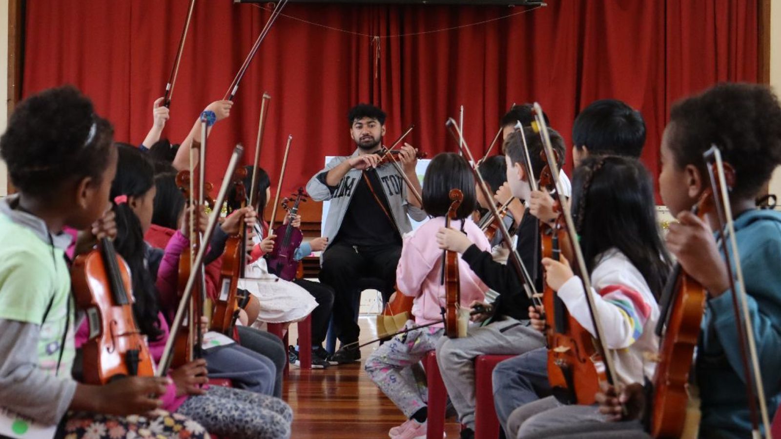 A man demonstrating how to use a violin to a group of children.