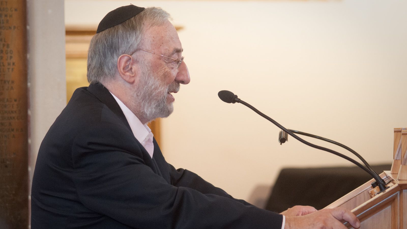 A profile shot of Dr Bernard Spolsky talking into a microphone at a lectern.