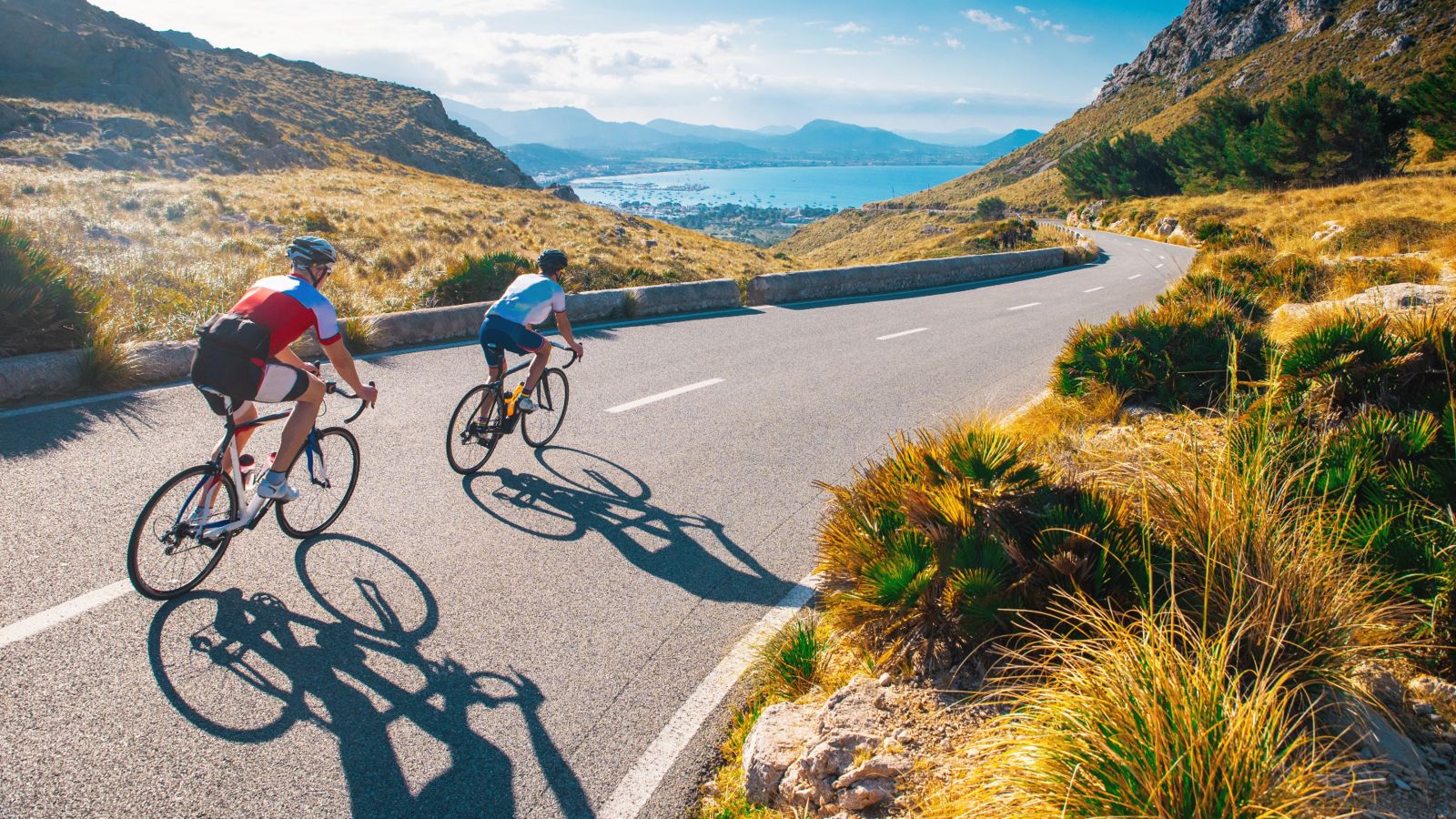 Two road cyclists in action with a beautiful bay in the background