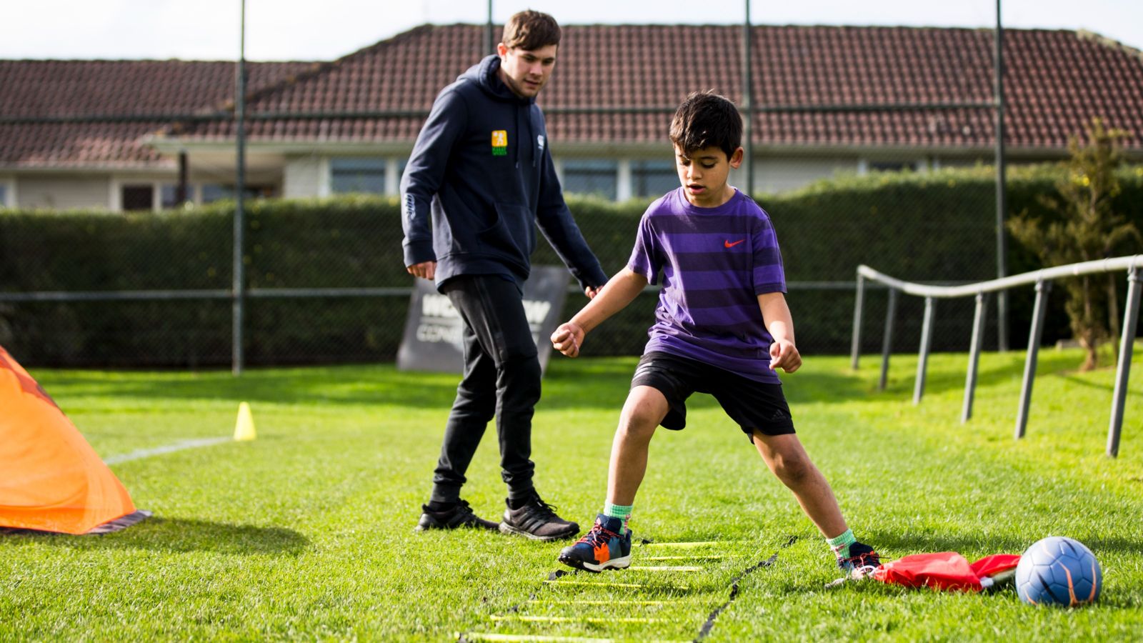 A child training on a field, with a coach behind them observing