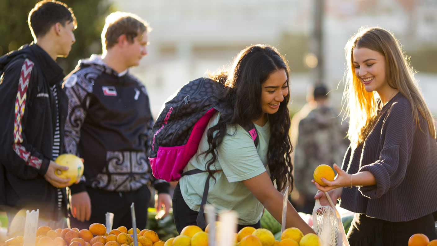 Smiling students choose fruit at an open air market.