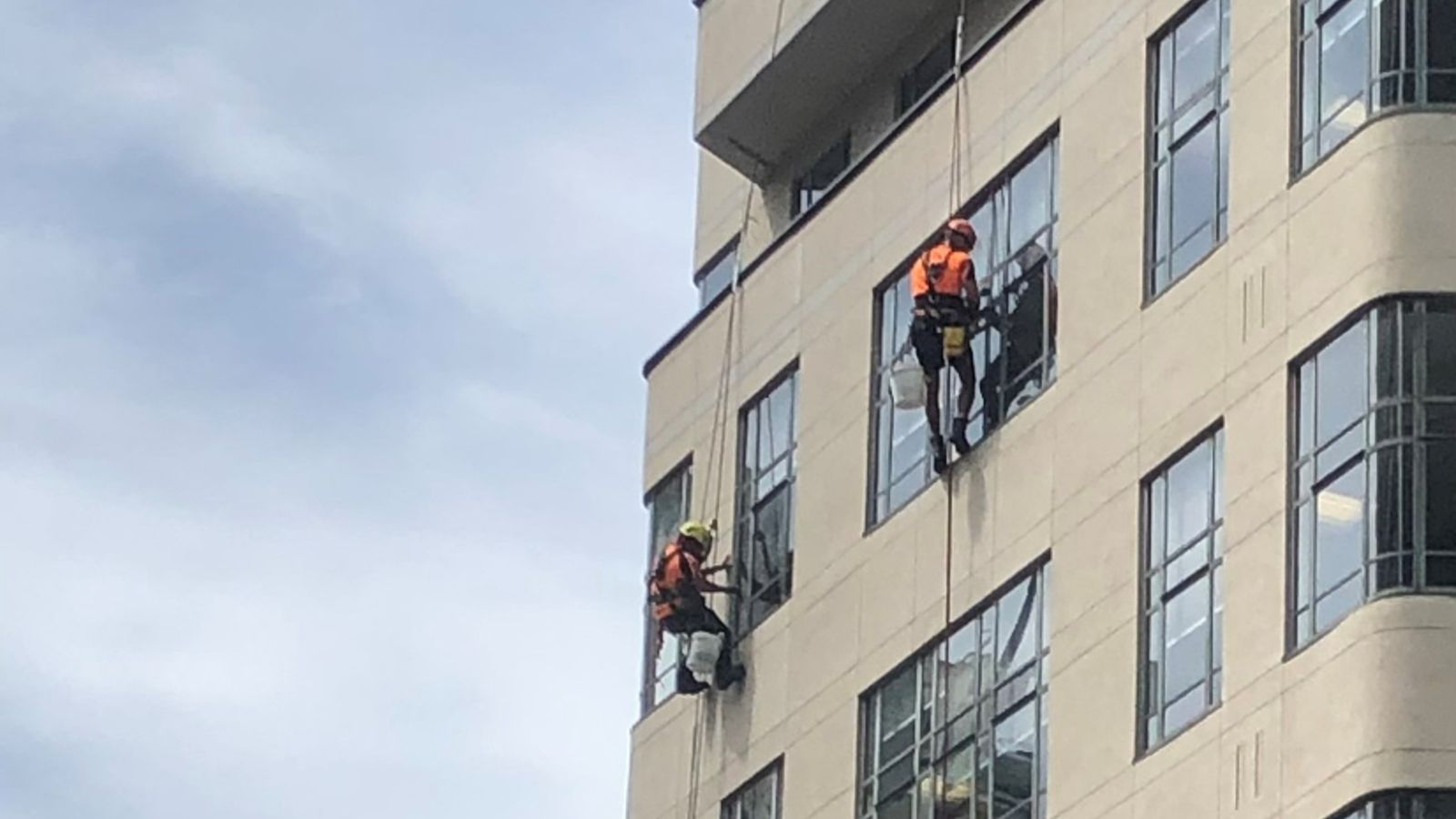 Two people abseiling from the roof of a building to clean the windows