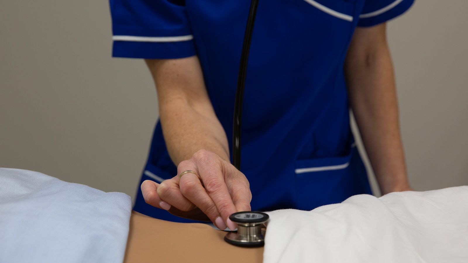 A nurse using a stethoscope on somebody's stomach