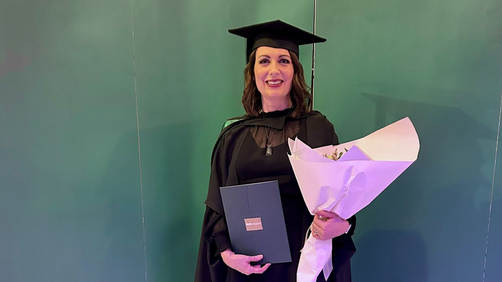 Ryl Jensen posing for a photo in her graduation attire. She is holding a bouquet of flowers.