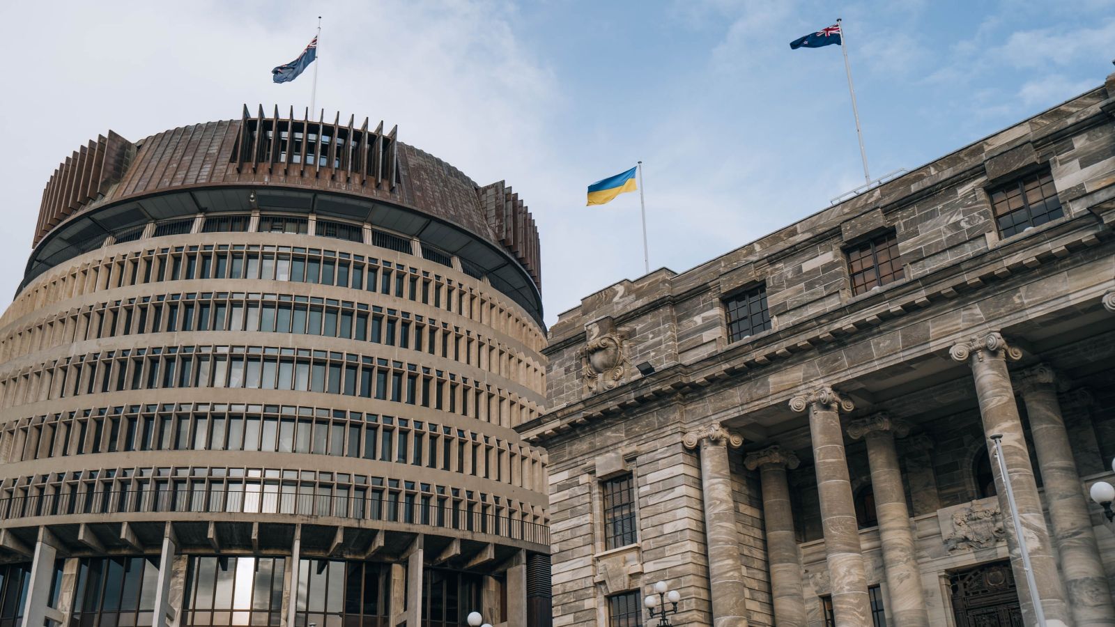 Circular building on left, old stone building on right, NZ flag on pole