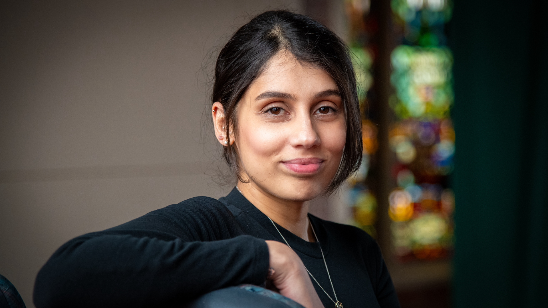 Nikitha looking into the camera in front of a stained glass window.