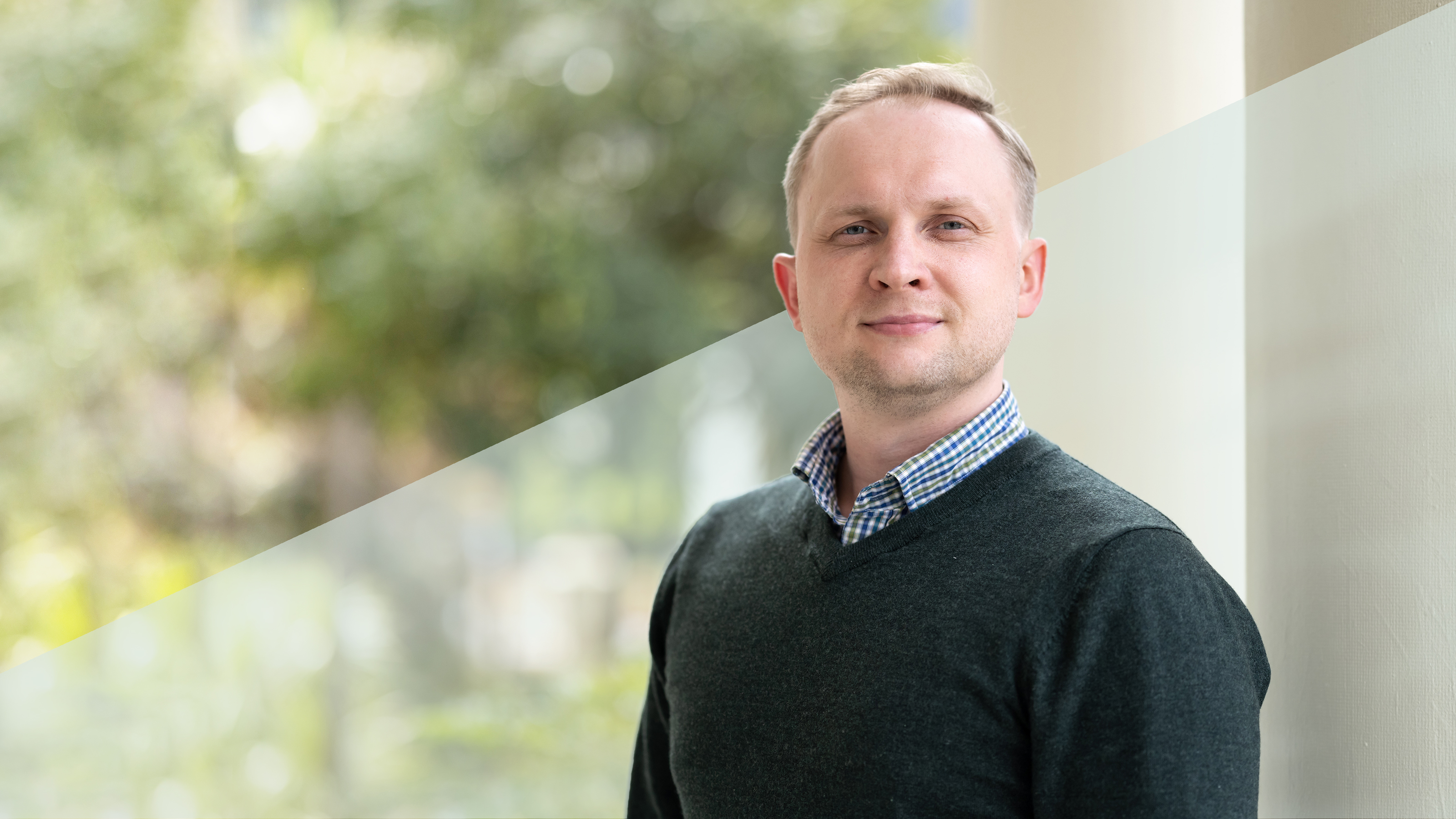 A profile of a man wearing a blue collared shirt and a black sweater.