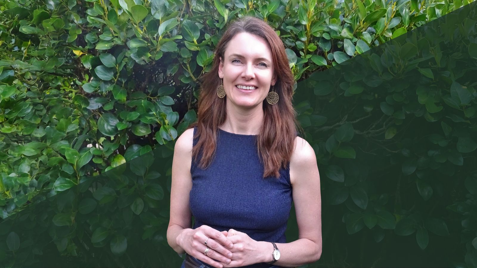 A woman in a purple dress standing in front of a large green hedge.