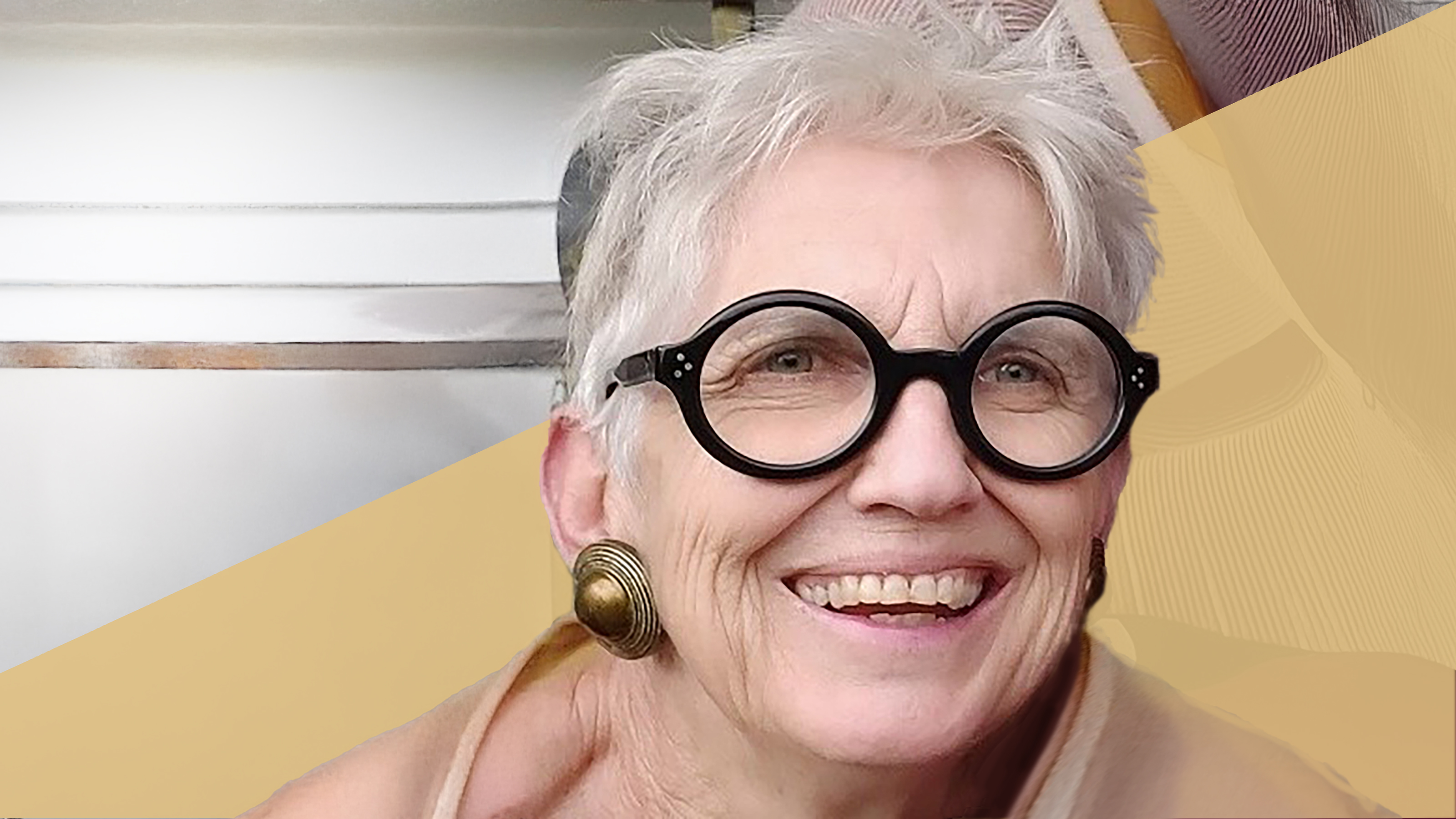 A close up of an older woman with glasses, smiling to the camera.