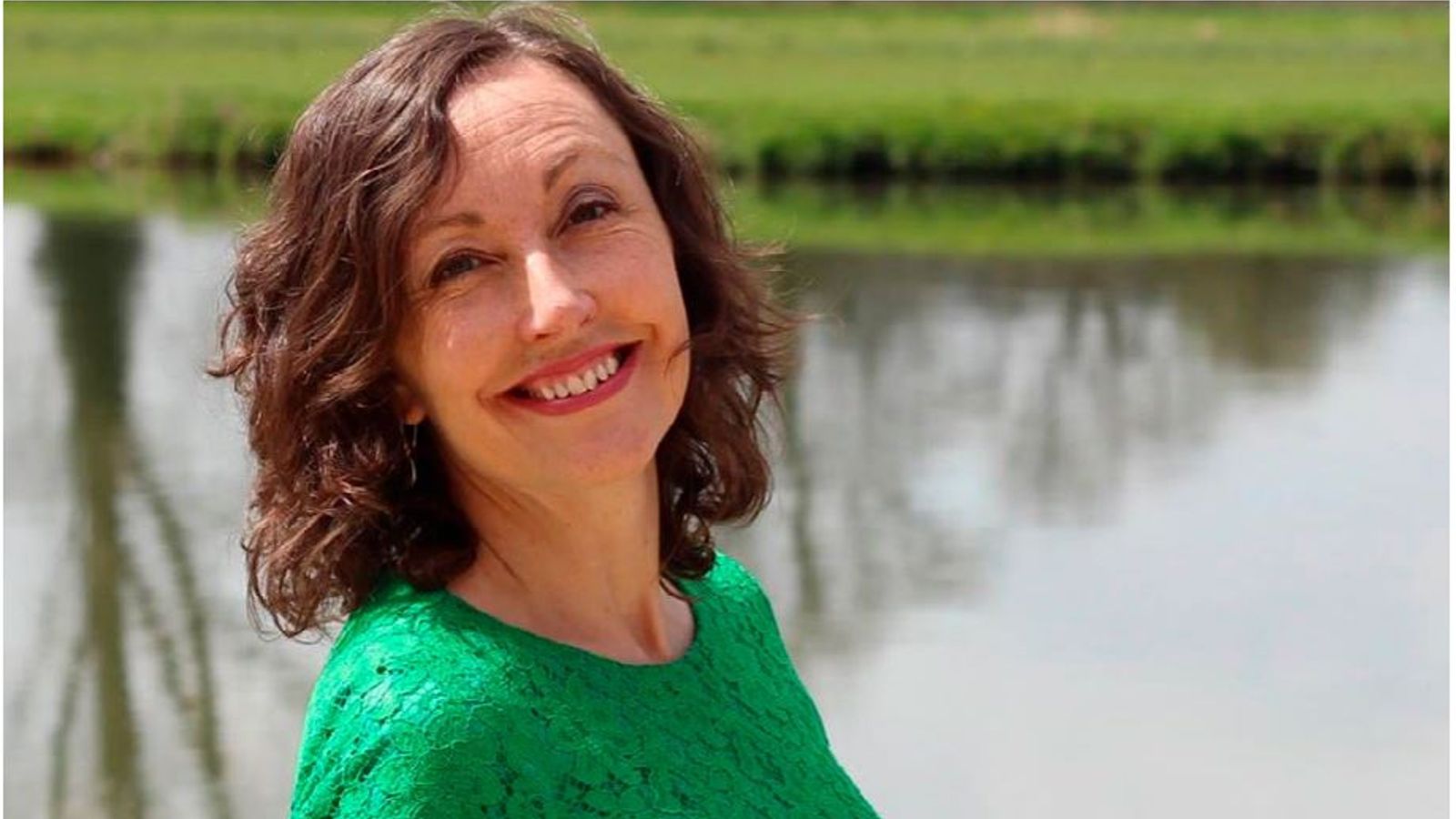Professor Aileen Kavanagh wears a green blouse and stands in front of a lake