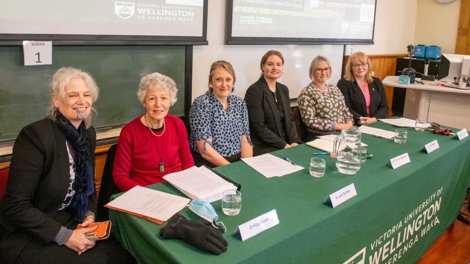 Six panelists sit at a long table 