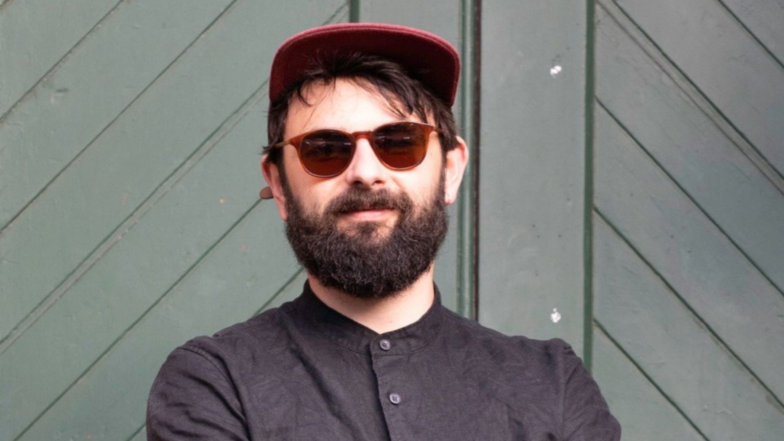 man with cap, beard, and sunglasses, wearing black button up shirt