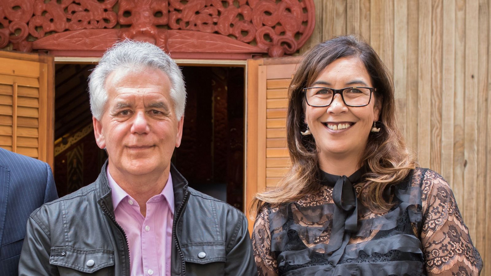 Man with grey hair and woman with dark hair in front of a marae door