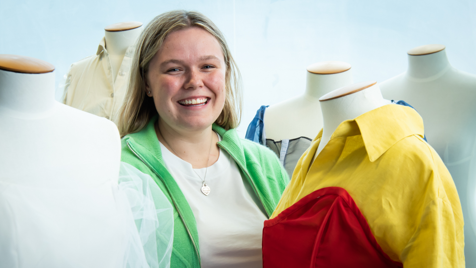 Lexie Etherington, a young woman, stands with her colorful designs displayed on mannequins.