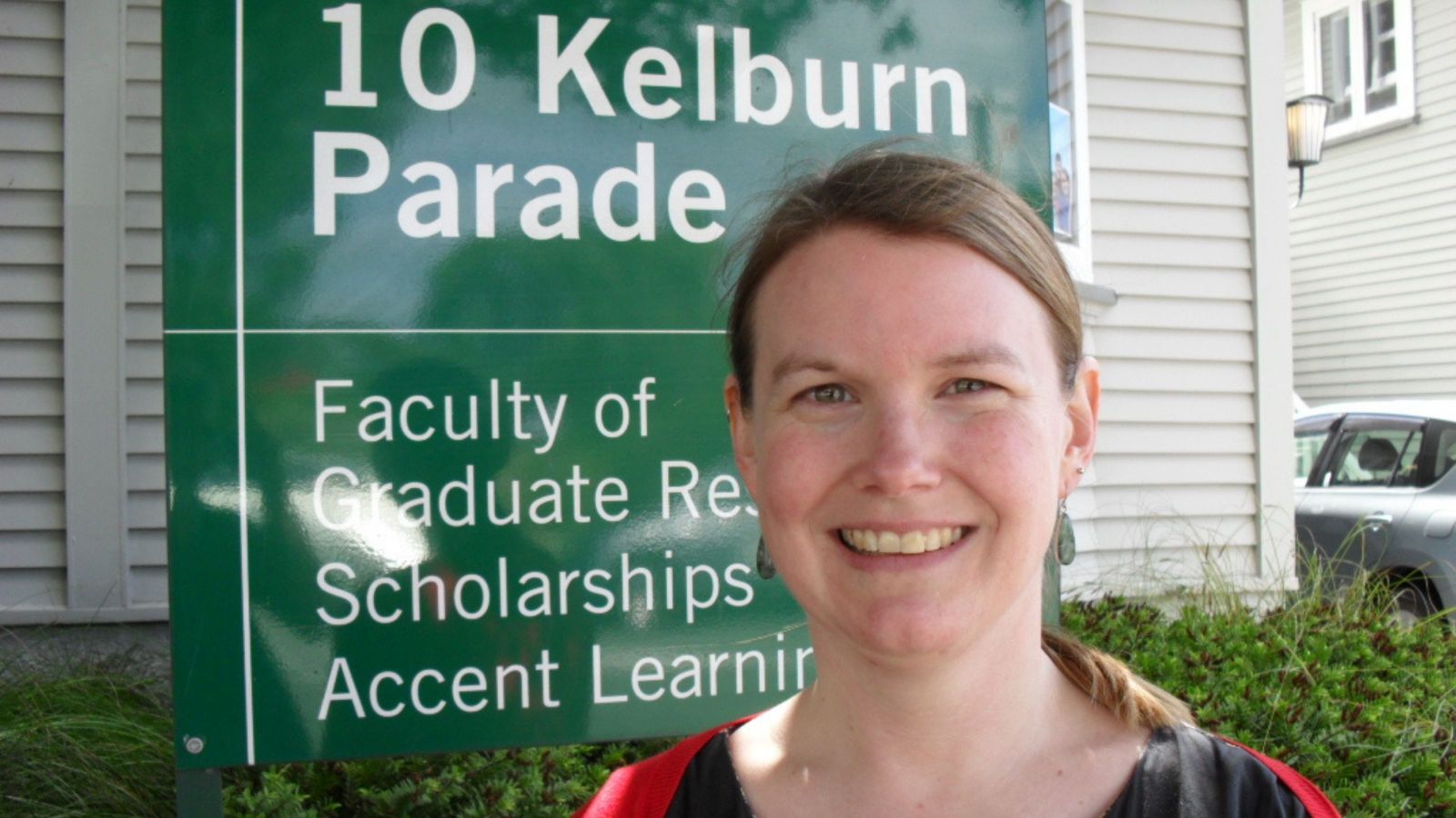 Girl with long blonde hair pulled back standing in front of a sign with 10 Kelburn Parade written on it