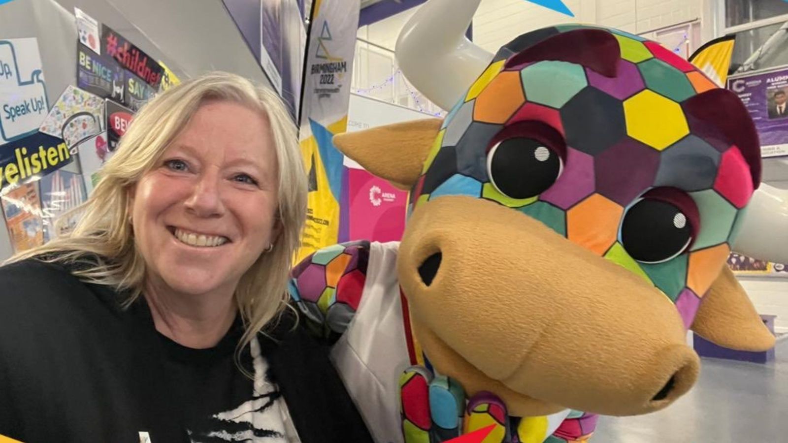 Woman with long blond hair with a colourful  stuffed cow mascot for the Birmingham Commonwealth Games