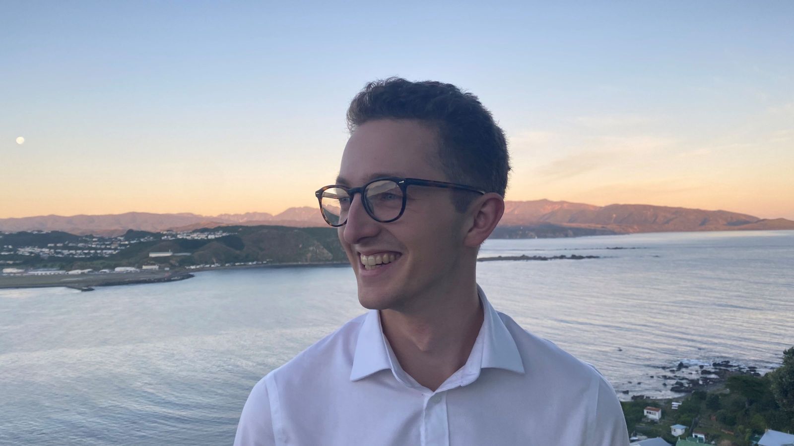 man with glasses looking sideways with sea and airport in background