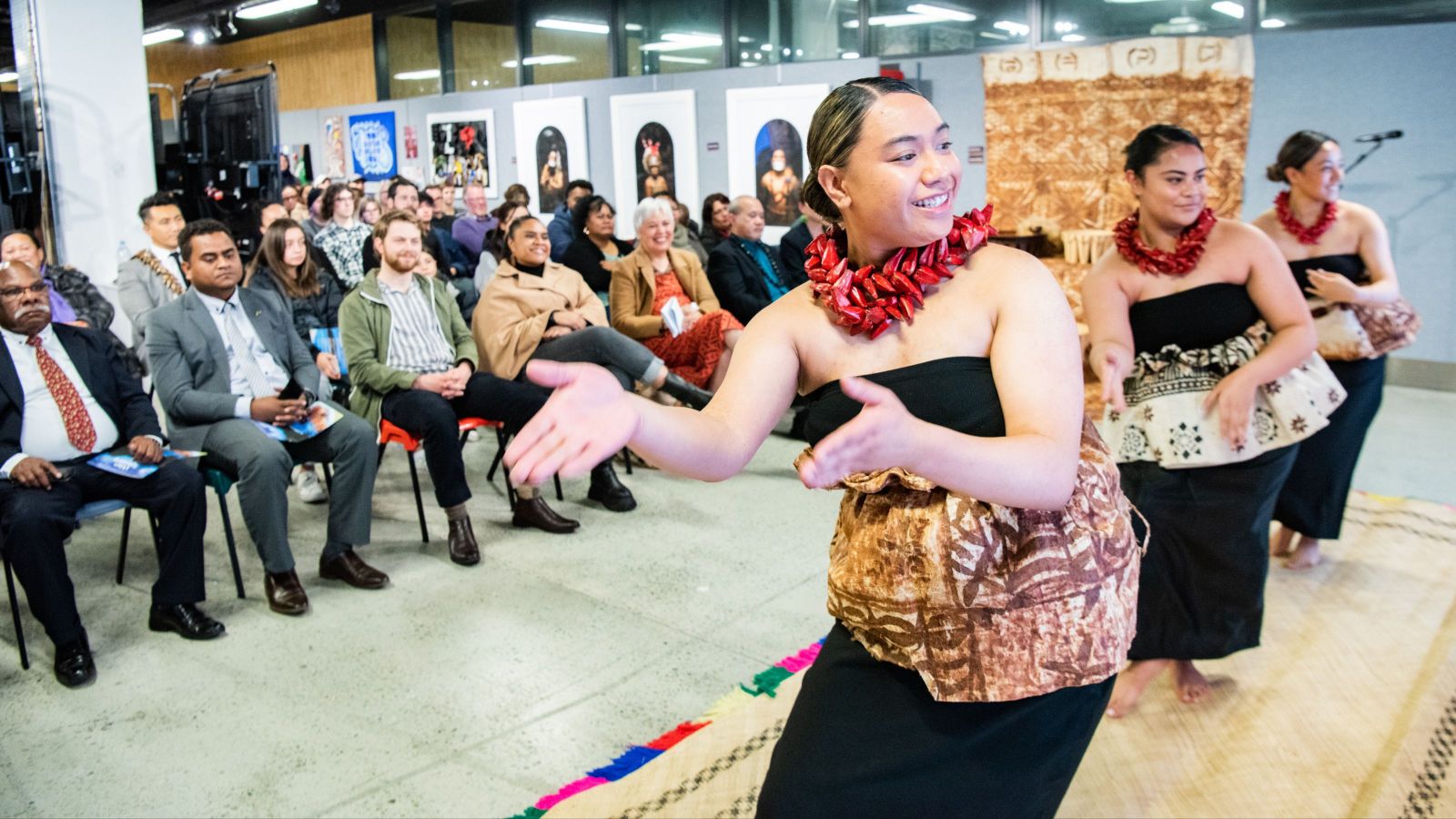 group of dancers in front of crowd with tapa cloth in background 