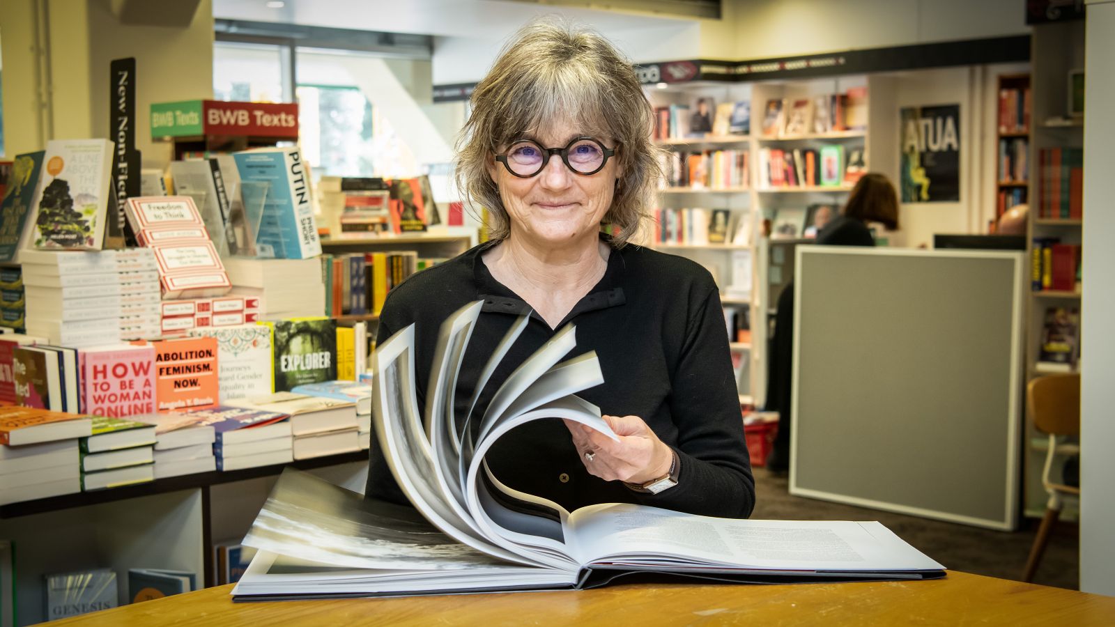 A woman with glasses flicks through a large book in a bookstore.