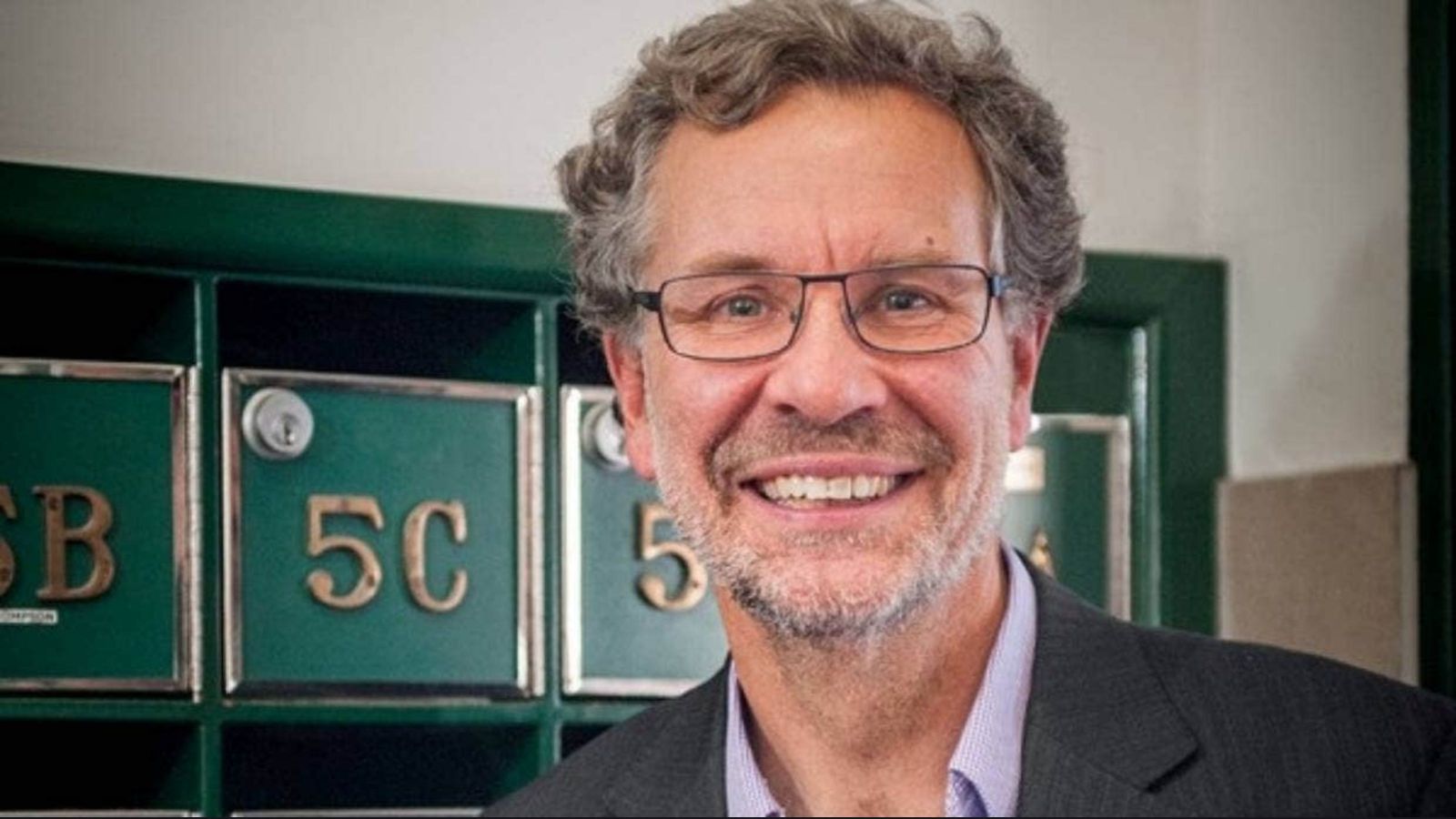 man with grey hair and goatee in front of green letterboxes