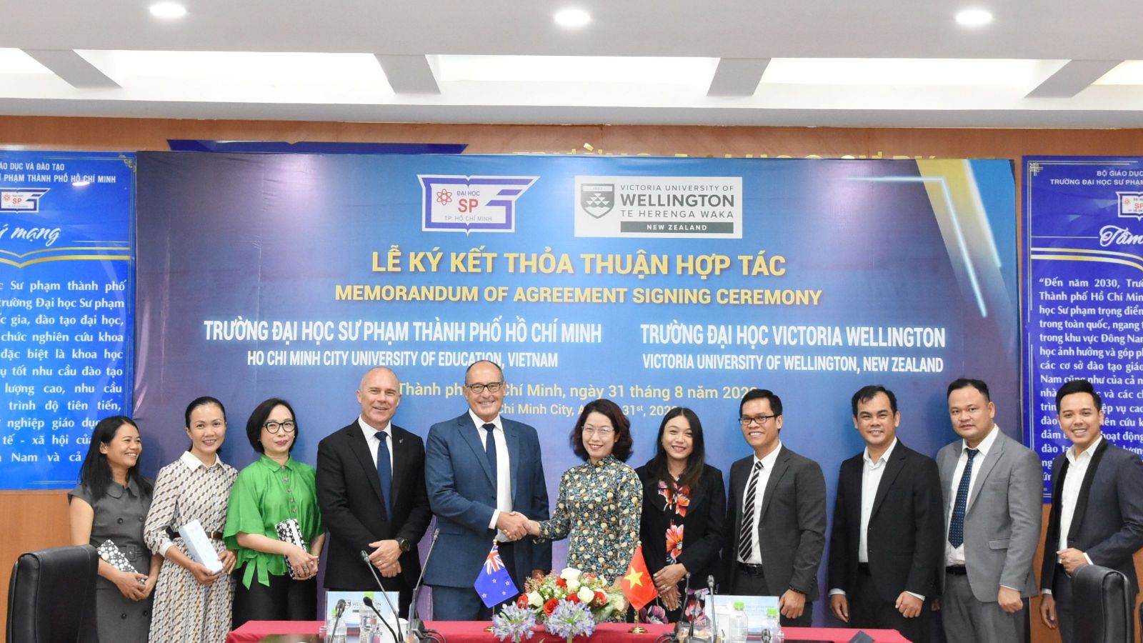 11 people standing in front of a formal poster with two shaking hands